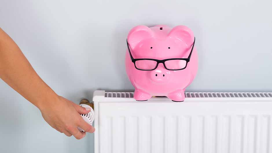 Person adjusting radiator with piggy bank on top Person adjusting radiator with piggy bank on top