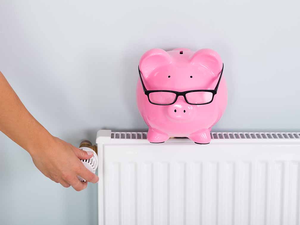 Person adjusting radiator with piggy bank on top Person adjusting radiator with piggy bank on top